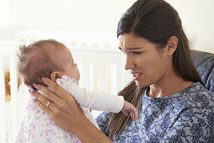 Photo of a stressed woman holding a baby, not knowing what could be wrong, she may need help with Post Natal Depression